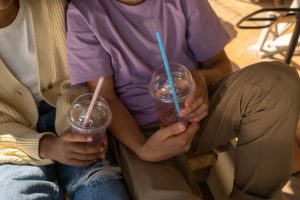 Of two young people holding their drinks which are in plastic cups with a straw in both. Their heads are not in the photo.