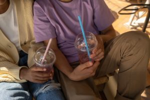 Of two young people holding their drinks which are in plastic cups with a straw in both. Their heads are not in the photo. 